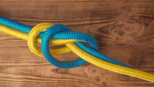海事或安全运动结绑扎过程 黄色和蓝色的绳子扭曲并绑在一起 形成结 隔离在木制背景上 近距离拍摄 两根绳子绑在一起 上视图 — 图库视频影像
