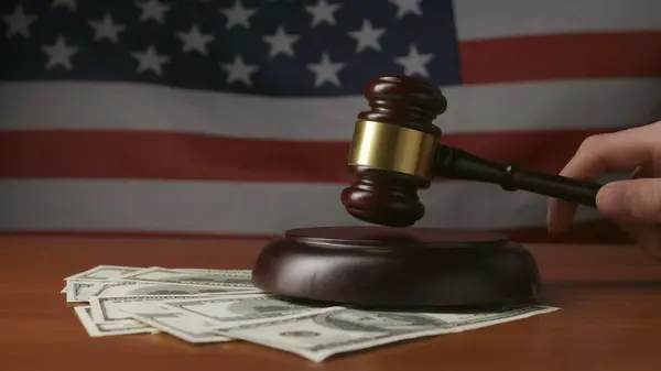 Masasında tahta tokmağı, dolar banknotları ve Amerikan bayrağı olan bir adam var. Mahkeme salonunda tahta bir tokmakla saldıran bir yargıç var. Yakın plan. Mahkeme ve rüşvet