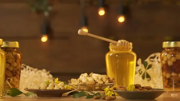 含有坚果的健康有机蜂蜜 玻璃瓶站在木制桌子上 上面放着新鲜的金黄色蜂蜜 蜂蜜调酒师躺在盛放着浓密糖浆 温暖阳光的大罐子上 图库照片
