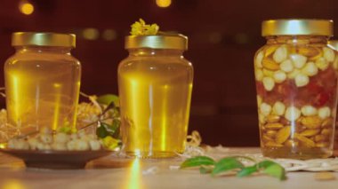 Fındıklı organik bal. Cam kavanozlar ahşap masanın üzerinde taze altın bal ile duruyor, fındıkla karıştırılmış kalın şurup, sıcak güneş ışığı yakın çekim.
