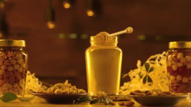 Fındıklı organik bal. Tahta masanın üzerinde duran cam kavanozlar taze altın bal, açık kavanozun üzerinde duran bal kapağı kalın şurup, sıcak güneş ışığı arka planı.