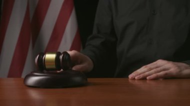 Hukuk ve adalet. Masasında tahta çekiç ve hukuk kitabıyla oturan erkek, arka planda ABD bayrağı. Mahkeme salonunda tahtadan tokmağa vurup yakın çekim yapan bir adam..