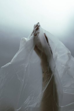 Perili bir görüntü, kısmen saf bir kumaş tarafından gizlenmiş bir insanı yakalıyor, gizemli ve ruhani bir hava yaratıyor, ince bir dövme ipucuyla..