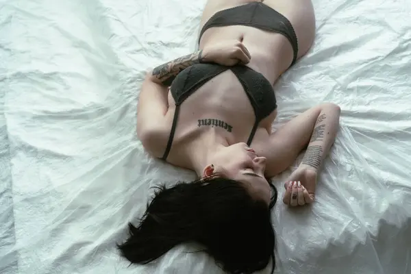 Жінка Татуюваннями Лежить Розслаблена Білому Ліжку Передаючи Спокійну Красу Стокове Зображення