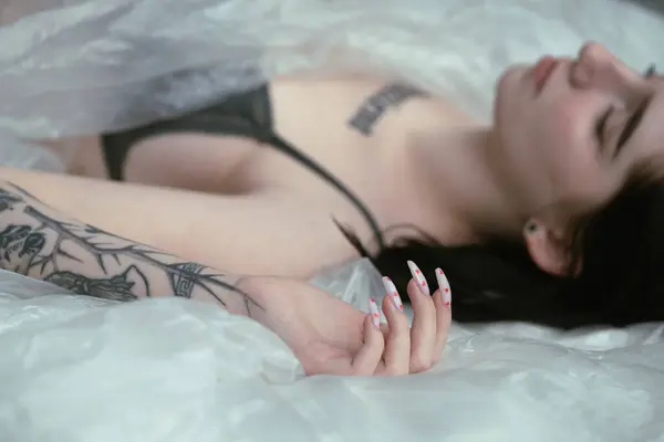 Женщина Татуировками Лежит Расслабленной Белой Кровати Передавая Безмятежную Красоту Стоковая Картинка