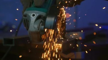 İşçi, çeliği kesmek için öğütücü makine kullanıyor. Sanayi fabrikasında öğütücüyle çalışan bir zanaatkar, demir boruların içinden geçen bir adam, atölyede kıvılcımlar uçuşuyor ve yere düşüyor..
