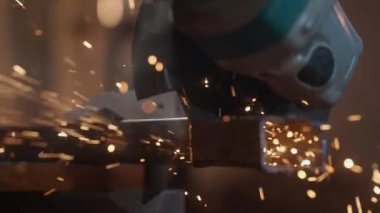 İşçi, çeliği kesmek için öğütücü makine kullanıyor. Sanayi fabrikasında öğütücüyle çalışan bir zanaatkar, demir boruların içinden geçen bir adam, atölyede kıvılcımlar uçuşuyor ve yere düşüyor..