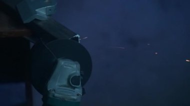 İşçi, çeliği kesmek için öğütücü makine kullanıyor. Sanayi fabrikasında öğütücüyle çalışan bir zanaatkar, demir parçalarının kıyısında çalışan bir adam, atölyede kıvılcımlar uçuşuyor ve yere düşüyor..