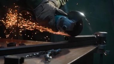 İşçi, çeliği kesmek için öğütücü makine kullanıyor. Sanayi fabrikasında öğütücüyle çalışan bir zanaatkar, demir parçalarının kıyısında çalışan bir adam, atölyede kıvılcımlar uçuşuyor ve yere düşüyor..