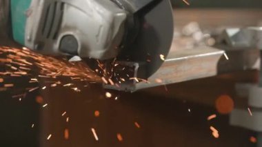 İşçi, çeliği kesmek için öğütücü makine kullanıyor. Sanayi fabrikasında öğütücüyle çalışan bir zanaatkar, demir parçalarının kıyısında çalışan bir adam, atölyede kıvılcımlar uçuşuyor ve yere düşüyor..