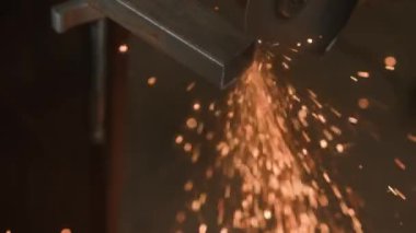 İşçi, çeliği kesmek için öğütücü makine kullanıyor. Sanayi fabrikasında öğütücüyle çalışan zanaatkar, demir parçaları öğüten adam, etrafta uçuşan ve atölyede yere düşen kıvılcımlar..