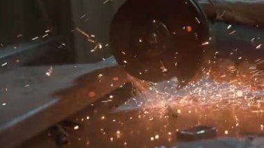 İşçi, çeliği kesmek için öğütücü makine kullanıyor. Sanayi fabrikasında öğütücüyle çalışan zanaatkar, demir parçaları öğüten adam, etrafta uçuşan ve atölyede yere düşen kıvılcımlar..
