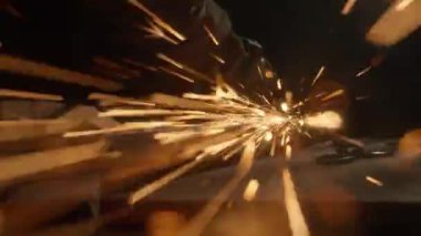 İşçi, çeliği kesmek için öğütücü makine kullanıyor. Koruyucu eldivenler giymiş bir zanaatkar endüstriyel fabrikada öğütücüyle çalışıyor demir parçaları öğütüyor, kamerada kıvılcımlar uçuşuyor..