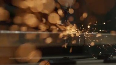 İşçi, çeliği kesmek için öğütücü makine kullanıyor. Koruyucu eldivenler giymiş bir zanaatkar endüstriyel fabrikada öğütücüyle çalışıyor demir parçaları öğütüyor, kamerada kıvılcımlar uçuşuyor..