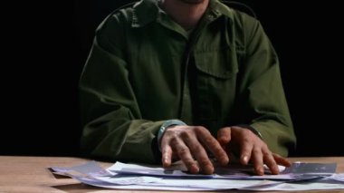 Hukuk ve adalet. Elleri kelepçeli bir erkek, mahkeme salonunda masada oturuyor, gergin bir ifade. Adam, suç davasının delillerine bakıyor. Fotoğraflara ve belgelere bakıyor..