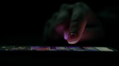 Düşük ışıkta bir akıllı telefon ekranında fotoğraf galerisinde kaydırılan bir parmağın yakın çekimi, aygıtların dokunmatik ekranla etkileşimini vurguluyor.