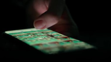 Düşük ışıkta bir akıllı telefon ekranında fotoğraf galerisinde kaydırılan bir parmağın yakın çekimi, aygıtların dokunmatik ekranla etkileşimini vurguluyor.