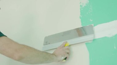 Duvarın yenilenmesi ve hazırlanması ile ilgili kesin çalışmaları gösteren bir mala kullanarak duvara macun uygulayan bir elin yakın plan görüntüsü. DIY ve inşaat temaları için ideal.
