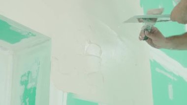 Duvarın yenilenmesi ve hazırlanması ile ilgili kesin çalışmaları gösteren bir mala kullanarak duvara macun uygulayan bir elin yakın plan görüntüsü. DIY ve inşaat temaları için ideal.