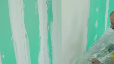 Duvarın yenilenmesi ve hazırlanması ile ilgili kesin çalışmaları gösteren bir mala kullanarak duvara macun uygulayan bir elin yakın plan görüntüsü. DIY ve inşaat temaları için ideal.