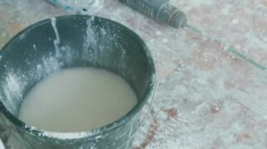 Kovada yoğurulmuş macun çözeltisi. Usta bir kovaya su ile macun tozu döker. İnşaat konusu, odada yenileme..