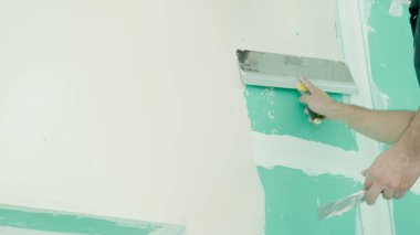 Duvarın yenilenmesi ve hazırlanması ile ilgili kesin çalışmaları gösteren bir mala kullanarak duvara macun uygulayan bir elin yakın plan görüntüsü. DIY ve inşaat temaları için ideal.