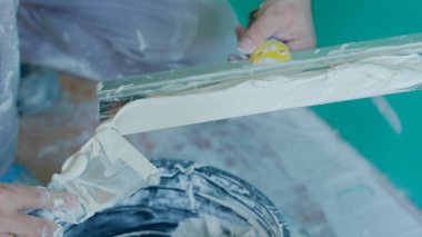 Bir inşaat işçisi macunu duvara sürmeden önce malaya yerleştirir. Bu yakın plan resim, pürüzsüz bir bitiş için gereken detayı ve hassasiyeti gösterir..