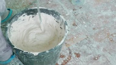 Bir inşaat işçisi macunu karıştırıcı aletle kovaya karıştırır. Bu resim, macunu duvar uygulamasına hazırlama sürecini yakalar, kullanılan araç ve gereçleri gösterir. Yavaş çekim