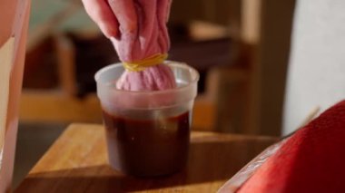 Eski tahta bir sandalyenin bacağına bez kullanarak leke süren bir kadının elini kapat. Bir atölyede ahşap işçiliği veya mobilya restorasyonu gösterisi.