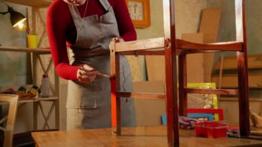 Bir atölyedeki ahşap sandalye yüzeyine kırmızı boya sürmek için fırça kullanan bir kadın boyama ve ahşap işçiliği sürecini gösteriyor..