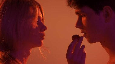 Genç erkek ve kadın şefkatli aşıklar, tutku dolu yakınlık dokunuşları, neşeli bir şekilde çilekle beslenen bir kadın. Aşk ve sevgi ilişkileri kavramı. Sevgili çift stüdyoda yakın çekim yapıyor..