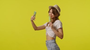 Dondurmalı günlük kıyafetlerle akıllı telefondan selfie çeken genç bir kadın. Seyahat, yaz tatili, turizm boş zaman konsepti. Kamera karşısında poz veren oyuncu kadın model sarı arka plan
