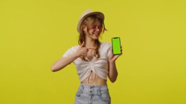 Akıllı telefon krom anahtar yeşil ekranında sıradan noktalarda genç bir kadın. Seyahat, yaz tatili, turizm boş zaman konsepti. Sarı arka planda izole edilmiş kameraya poz veren oyuncu genç bayan model.