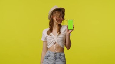 Gündelik akıllı telefon kroma anahtar yeşil ekranlı genç bir kadın. Seyahat, yaz tatili, turizm boş zaman konsepti. Sarı arka planda izole edilmiş kameraya poz veren oyuncu genç bayan model..