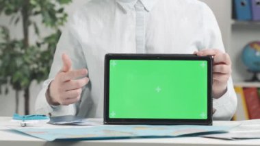 Bir seyahat acentesi elinde yeşil ekranlı bir tablet tutuyor ve ekranı işaret ediyor. Metin veya resim için şablon yeri, promosyon içeriği. Reklam alanı, çalışma alanı maketi.