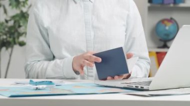 Bir seyahat acentesinin elleri dizüstü bilgisayarda yazı yazarken ve bilet ya da otel ayırtırken pasaport bilgilerini girerken yakın plan. Modern seyahat rezervasyon hizmetlerinin dijital ve çevrimiçi yönü.