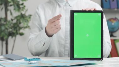 Bir seyahat acentesi elinde yeşil ekranlı bir tablet tutuyor ve ekranı işaret ediyor. Metin veya resim için şablon yeri, promosyon içeriği. Reklam alanı, çalışma alanı maketi.