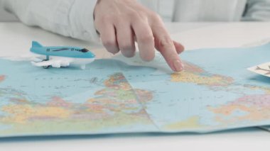 Dünya haritasını işaret eden ve seyahat seçeneklerine bakan bir kadın seyahat acentesinin yakın çekimi. Tatil planlama, seyahat için bir ülke seçme, turne rezervasyonu, biletler ve oteller.