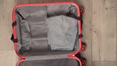 Kadın eli, şeftali rengi bavul taşır. Çanta bir şapka, sandalet, kot pantolon ve renkli gömlekler de dahil olmak üzere yaz kıyafetleriyle dolu..