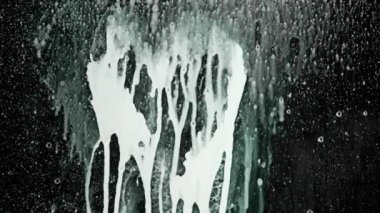 Sanatçı şeffaf cam yüzeyde çizim yapar. Siyah cam ekran üzerine köpük püskürten kişi kalp işareti çizerek izole edilmiş. Yağlı akrilik boya, aşağı doğru akan sıvı, zıt manzara..