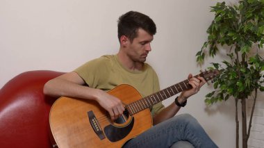 Evde gitar çalan genç bir müzisyen. Yetişkin bir gitarist odada oturup akustik gitar çalıyor, melodi besteleyip, akorları parmaklıyor. Hobi ve boş zaman kavramı.