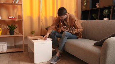 Evde gitar çalan genç bir müzisyen. Yetişkin bir gitarist odada oturup akustik gitar çalıyor, beste yapıyor ve nota kağıdına yazıyor. Hobi ve boş zaman kavramı.