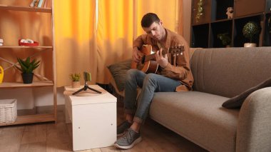 Evde gitar çalan genç bir müzisyen. Yetişkin gitarist odada oturmuş akustik gitar çalıyor ve akıllı telefon öğrenme dersleri alıyor. Hobi ve boş zaman kavramı.