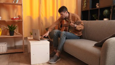 Evde gitar çalan genç bir müzisyen. Yetişkin bir gitarist odada oturmuş akustik gitar çalıyor. İnternette dizüstü bilgisayar öğrenme dersleri alıyor. Hobi ve boş zaman kavramı.