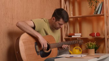 Evde gitar çalan genç bir müzisyen. Yetişkin bir gitarist odada oturup akustik gitar çalıyor, beste yapıyor ve nota kağıdına yazıyor. Hobi ve boş zaman kavramı.