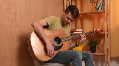 Evde gitar çalan genç bir müzisyen. Yetişkin bir gitarist odada oturup akustik gitar çalar, melodi besteler, akorları çalar, düşünür. Hobi ve boş zaman kavramı.