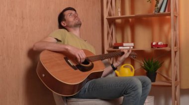 Evde gitar çalan genç bir müzisyen. Yetişkin bir gitarist odada oturup akustik gitar çalar, melodi besteler, akorları çalar, düşünür. Hobi ve boş zaman kavramı.