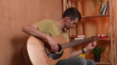 Evde gitar çalan genç bir müzisyen. Yetişkin gitarist odada oturup akustik gitar çalıyor, telleri sıkıyor ve enstrümanı kuruyor. Hobi ve boş zaman kavramı.