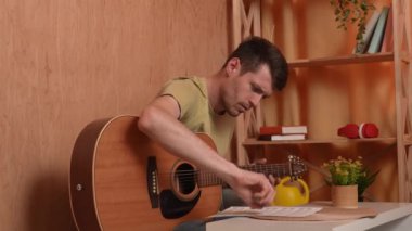 Evde gitar çalan genç bir müzisyen. Yetişkin bir gitarist odada oturup akustik gitar çalıyor, beste yapıyor ve nota kağıdına yazıyor. Hobi ve boş zaman kavramı.