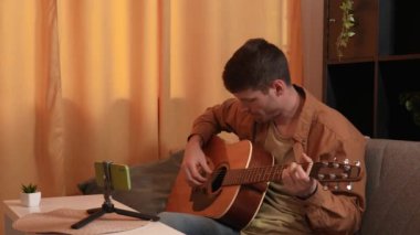 Evde gitar çalan genç bir müzisyen. Yetişkin gitarist odada oturmuş akustik gitar çalıyor ve akıllı telefon öğrenme dersleri alıyor. Hobi ve boş zaman kavramı.